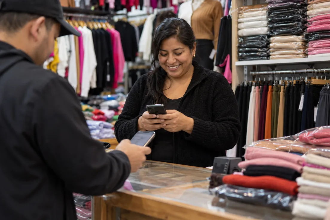 Comerciante peruana recibiendo el pago de un cliente en su tienda de ropa del Brás